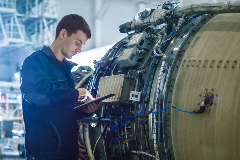 Aircraft maintenance mechanic inspecting and working on airplane jet engine in hangar