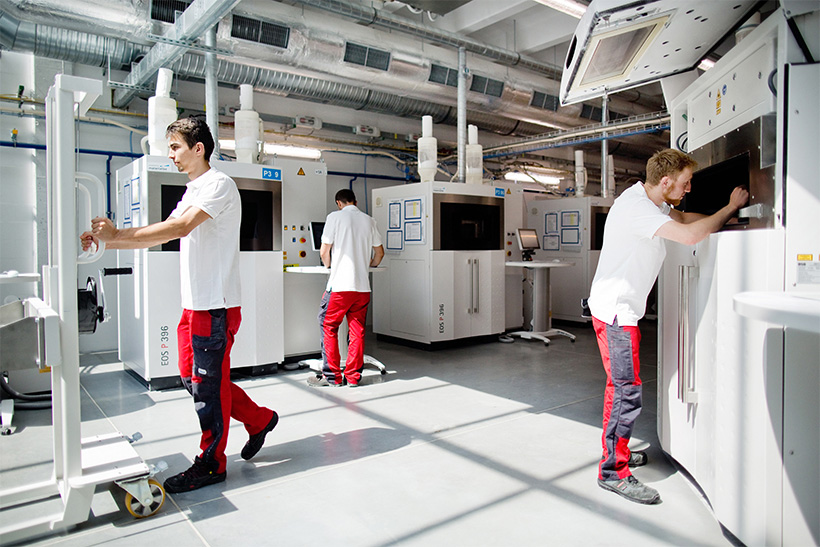 Three production operators work on 3D printing machines in a Selective Laser Sintering facility