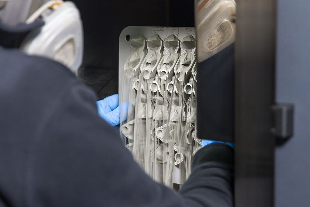 Operator produkcji części z metalu w zakładzie drukowania 3D z metalu firmy Materialise rozpoczyna procesy obróbki końcowej